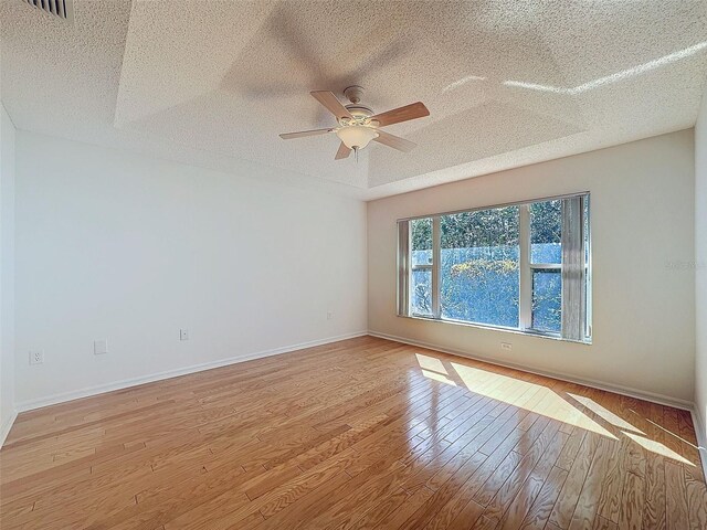 empty room featuring visible vents, light wood-style floors, ceiling fan, a textured ceiling, and baseboards