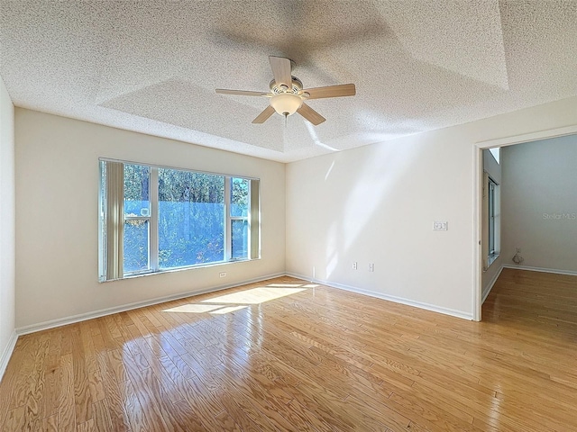 spare room featuring a textured ceiling, ceiling fan, light wood finished floors, and baseboards