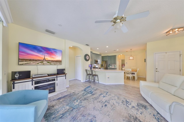 living area with visible vents, arched walkways, a ceiling fan, a textured ceiling, and a fireplace