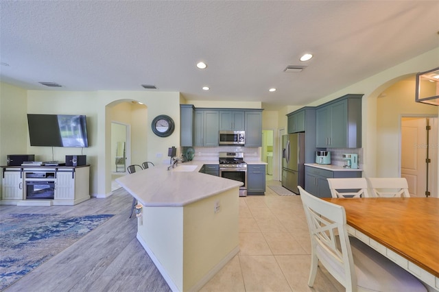 kitchen featuring a peninsula, arched walkways, stainless steel appliances, and a sink