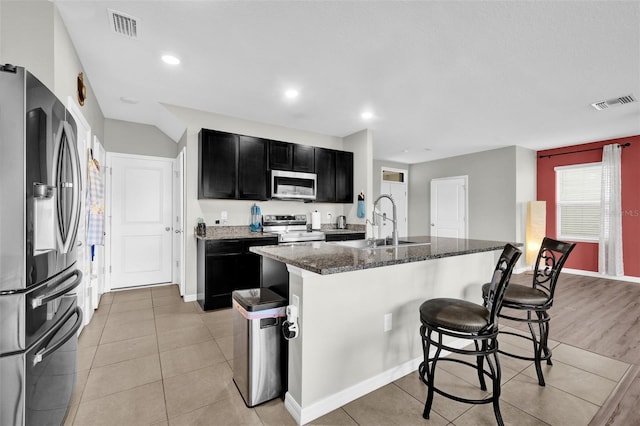 kitchen with stainless steel appliances, dark cabinetry, visible vents, and a kitchen bar