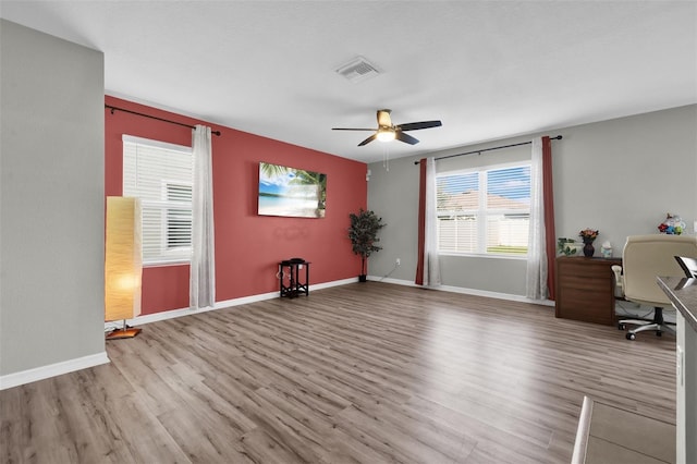 interior space featuring a ceiling fan, visible vents, baseboards, and wood finished floors