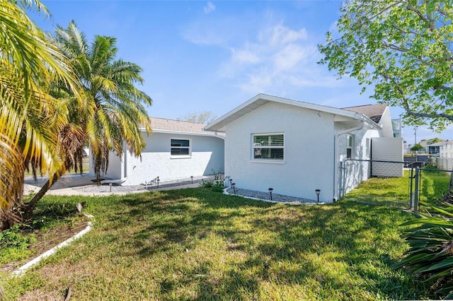 rear view of property featuring a gate, a lawn, fence, and stucco siding