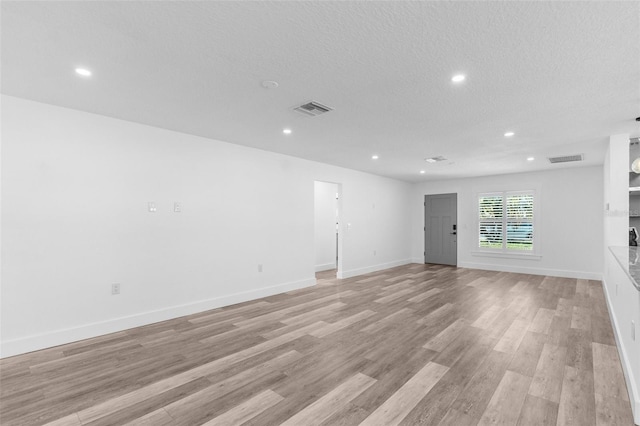 unfurnished room featuring light wood-style floors, baseboards, visible vents, and a textured ceiling