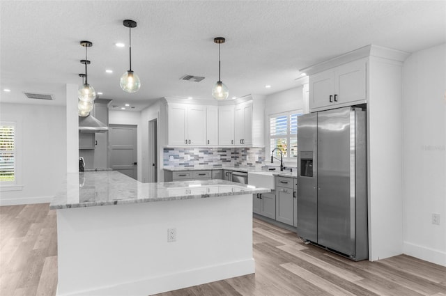 kitchen with stainless steel appliances, a peninsula, a sink, visible vents, and tasteful backsplash