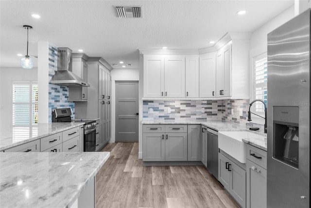 kitchen featuring light wood finished floors, stainless steel appliances, visible vents, a sink, and wall chimney range hood