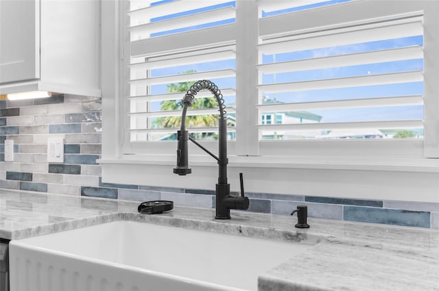 details with tasteful backsplash, white cabinets, light stone countertops, stainless steel dishwasher, and a sink