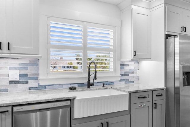 kitchen with stainless steel appliances, a sink, white cabinetry, backsplash, and light stone countertops