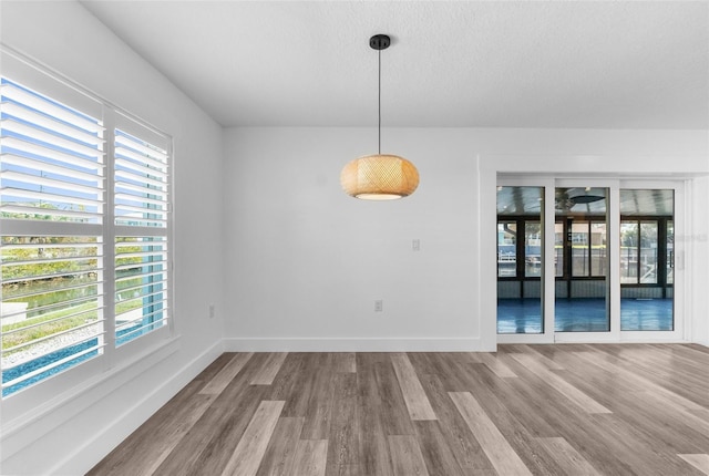 unfurnished dining area with wood finished floors, a wealth of natural light, and baseboards