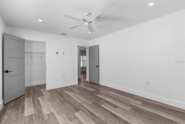 unfurnished bedroom with wood finished floors, a ceiling fan, baseboards, a closet, and a walk in closet