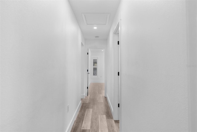 hall featuring light wood finished floors, attic access, and baseboards