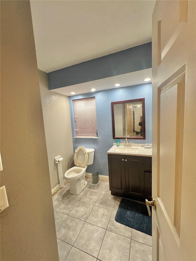 half bath featuring a textured wall, tile patterned flooring, toilet, vanity, and baseboards