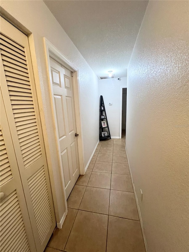 hall with a textured wall, a textured ceiling, baseboards, and tile patterned floors