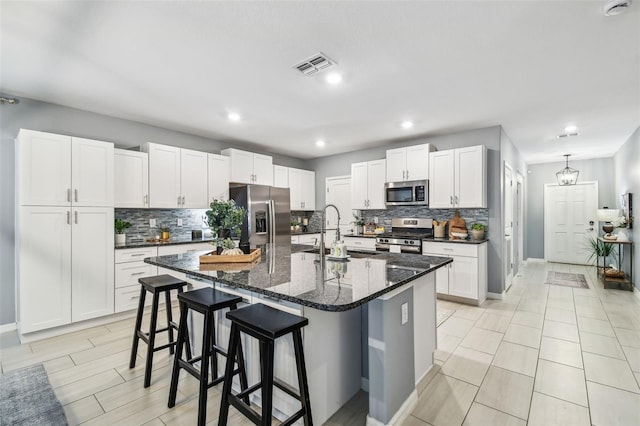 kitchen with visible vents, a breakfast bar, a kitchen island with sink, a sink, and stainless steel appliances