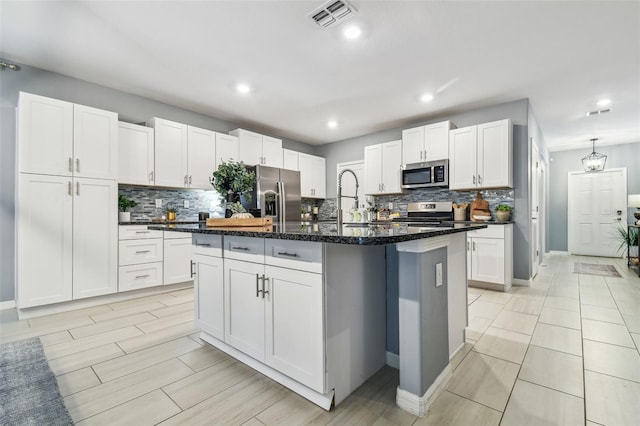 kitchen featuring visible vents, a center island with sink, white cabinets, stainless steel appliances, and a sink