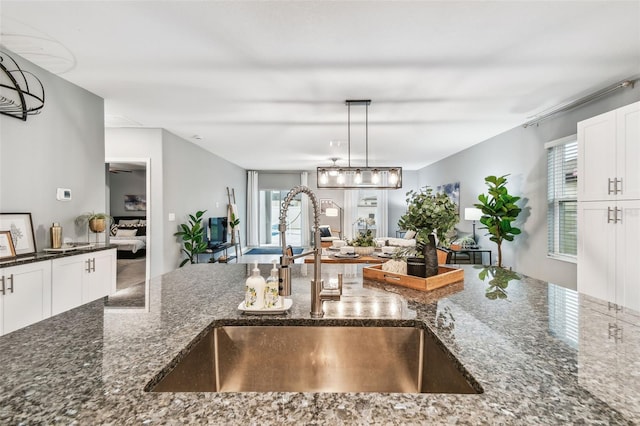 kitchen featuring dark stone countertops, a sink, pendant lighting, white cabinetry, and open floor plan