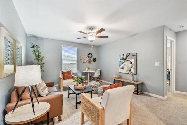 living area with baseboards, light carpet, and a ceiling fan