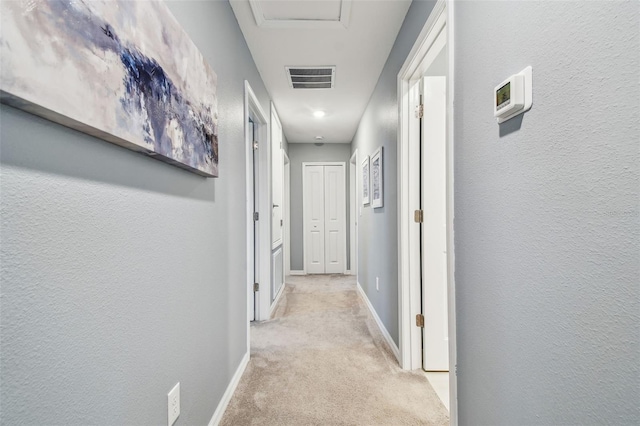 hall featuring baseboards, a textured wall, visible vents, and light carpet