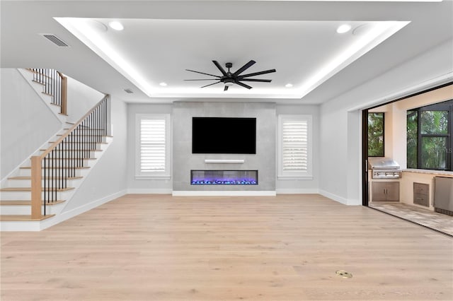 unfurnished living room with plenty of natural light, a tray ceiling, light wood-type flooring, and visible vents