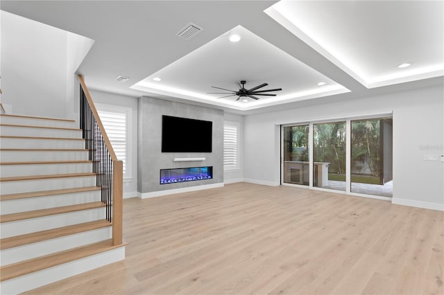 unfurnished living room with stairway, a raised ceiling, light wood-style flooring, and a ceiling fan