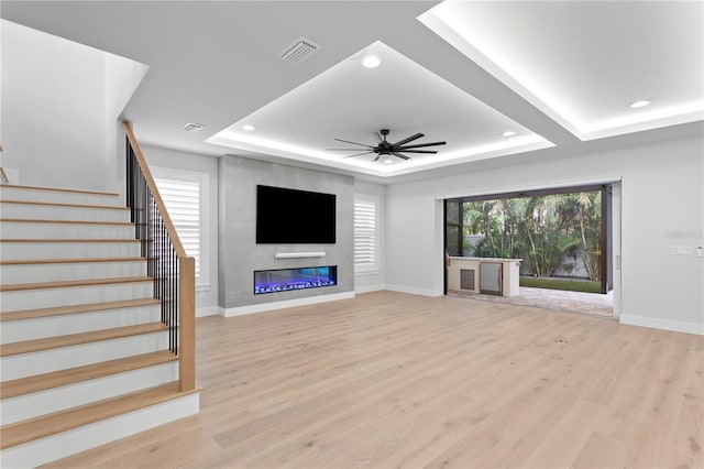 unfurnished living room featuring light wood-type flooring, a raised ceiling, visible vents, and stairway