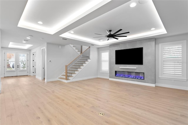 unfurnished living room featuring light wood-type flooring, a raised ceiling, and stairway