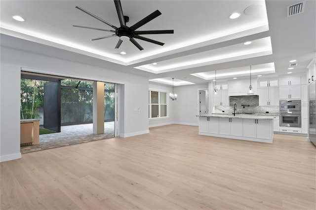 unfurnished living room with a sink, a raised ceiling, visible vents, and light wood-style floors