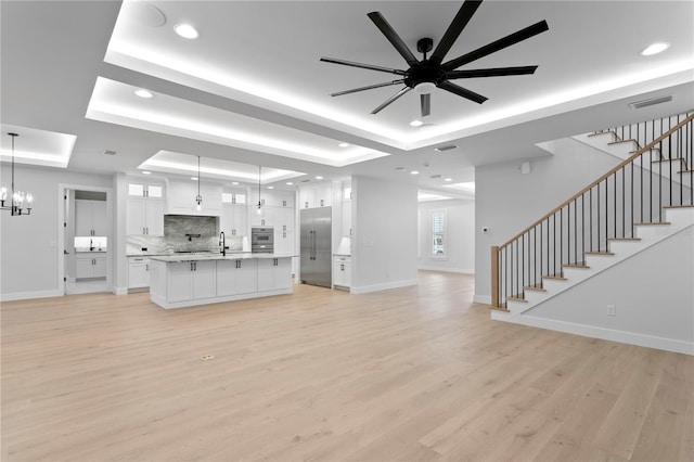 unfurnished living room with baseboards, visible vents, a raised ceiling, stairs, and light wood-style floors