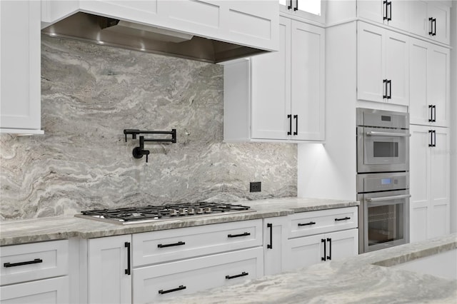 kitchen with stainless steel appliances, white cabinets, premium range hood, and tasteful backsplash