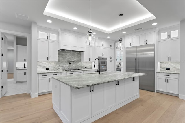 kitchen with stainless steel appliances, a raised ceiling, white cabinetry, and a sink