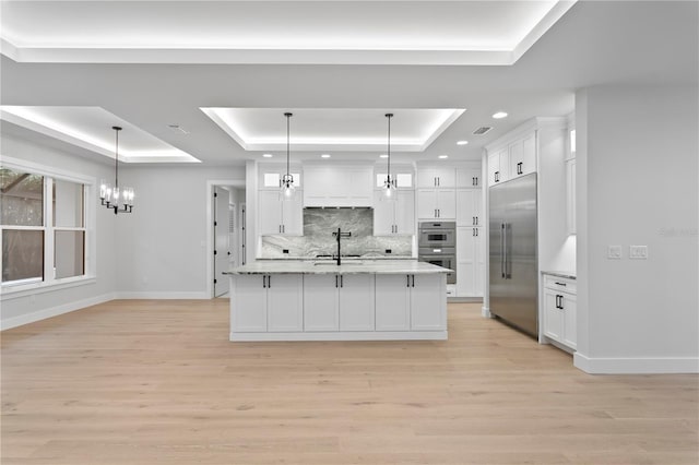 kitchen with light wood finished floors, a raised ceiling, appliances with stainless steel finishes, white cabinetry, and a sink