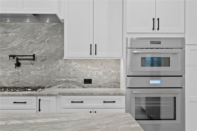 kitchen featuring wall chimney exhaust hood, light stone counters, stainless steel appliances, and backsplash