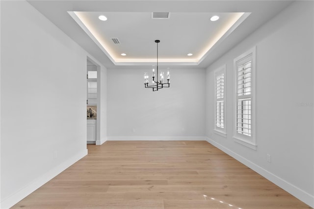 unfurnished dining area featuring a tray ceiling, visible vents, light wood-style flooring, and baseboards