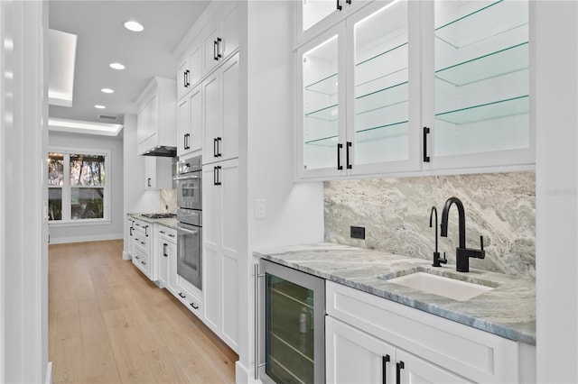 kitchen featuring light stone counters, light wood-style floors, white cabinets, a sink, and beverage cooler