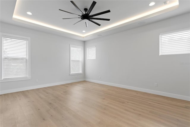 spare room with light wood-style floors, baseboards, a raised ceiling, and recessed lighting