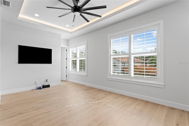 unfurnished living room featuring a raised ceiling, visible vents, baseboards, and light wood finished floors