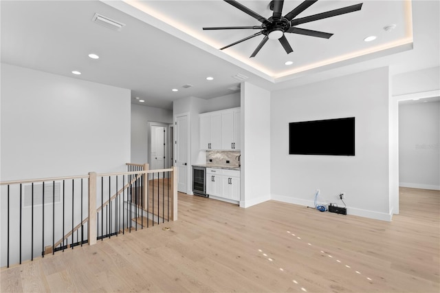 living area featuring a tray ceiling, recessed lighting, light wood-type flooring, beverage cooler, and baseboards