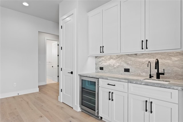 bar with light wood finished floors, tasteful backsplash, a sink, beverage cooler, and baseboards