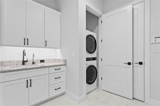 laundry area featuring laundry area, stacked washer / dryer, a sink, baseboards, and marble finish floor