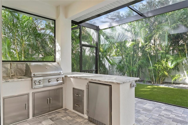 view of patio / terrace featuring glass enclosure, an outdoor kitchen, a sink, and area for grilling