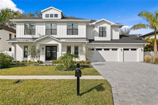 modern inspired farmhouse featuring decorative driveway, an attached garage, board and batten siding, a front yard, and a standing seam roof