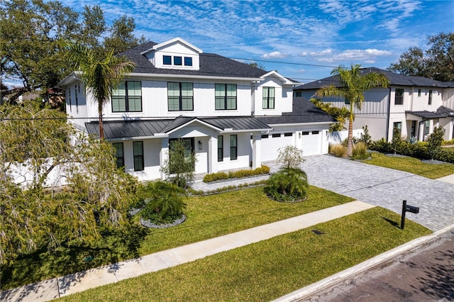 modern farmhouse featuring a garage, a shingled roof, a standing seam roof, decorative driveway, and a front lawn