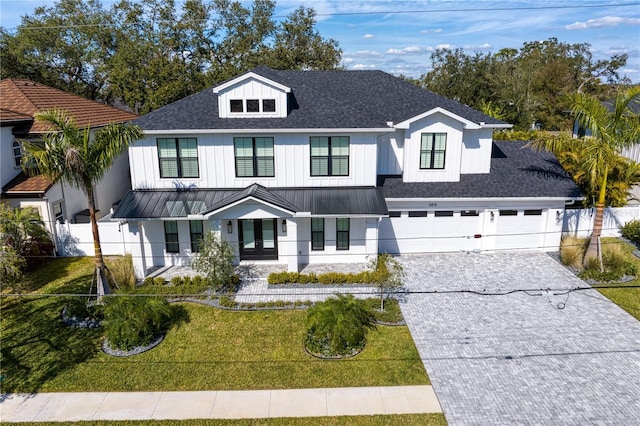 modern farmhouse style home with an attached garage, fence, roof with shingles, decorative driveway, and a front lawn