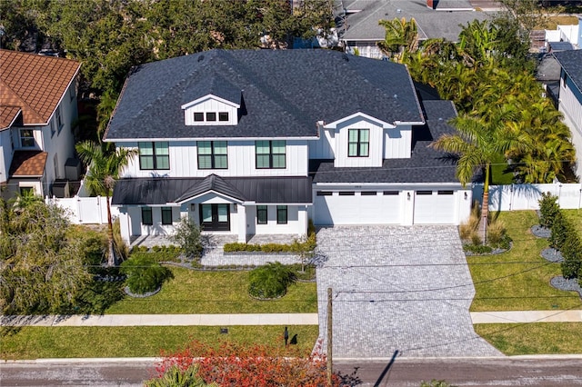 modern inspired farmhouse with concrete driveway, an attached garage, a standing seam roof, fence, and a front yard