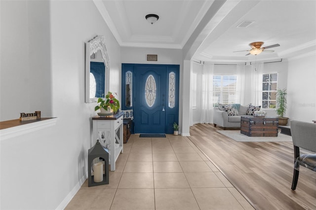 tiled entrance foyer featuring a tray ceiling, visible vents, ornamental molding, a ceiling fan, and baseboards