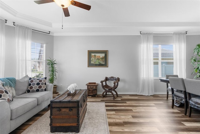 living area featuring baseboards, a ceiling fan, ornamental molding, wood finished floors, and a tray ceiling