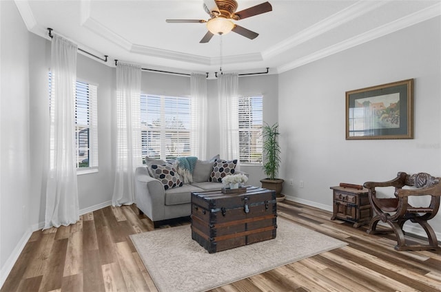 living room featuring ornamental molding, a raised ceiling, baseboards, and wood finished floors