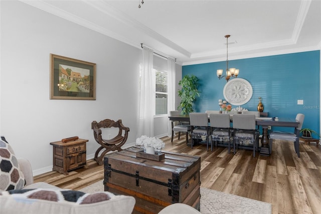 living area featuring a raised ceiling, ornamental molding, wood finished floors, and a notable chandelier