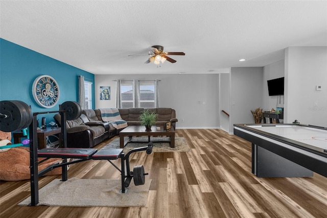 living area with a ceiling fan, a textured ceiling, baseboards, and wood finished floors