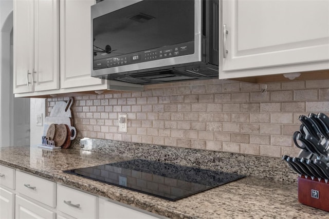 kitchen with black electric stovetop, stainless steel microwave, white cabinetry, and decorative backsplash